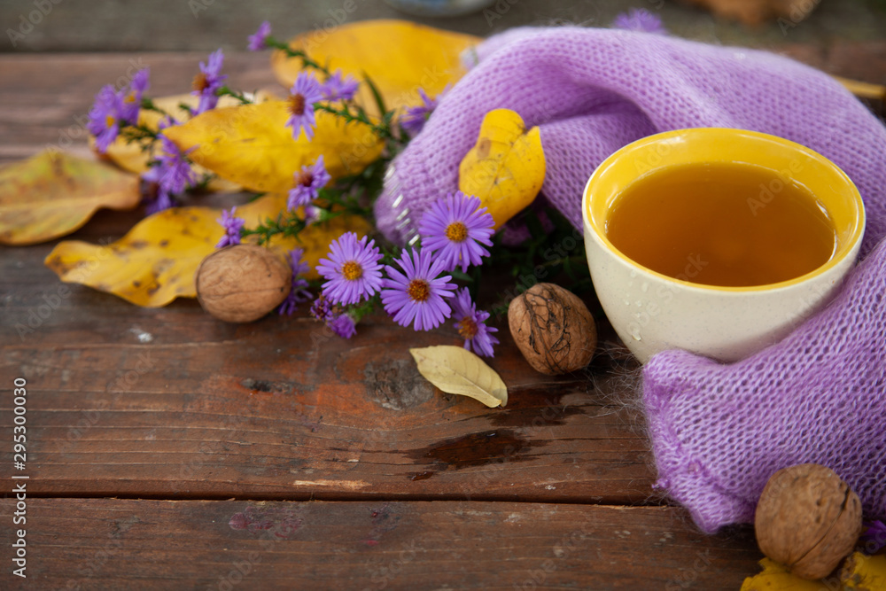 Cropped photo of a white cup with tea and a violet sweater strewn with orange maple leaves on a wooden table. The concept of comfort, coziness and hygiene. Cropped photo of a white cup with tea and a violet sweater strewn with orange maple leaves on a wooden table. The concept of comfort, coziness and hygiene.