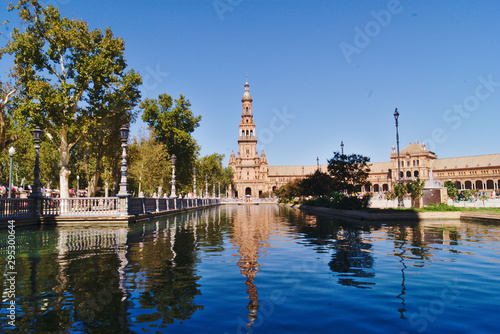 Views of the Seville Plaza de Espana from the side, where the main tower is reflected in the water of the canal on a sunny day