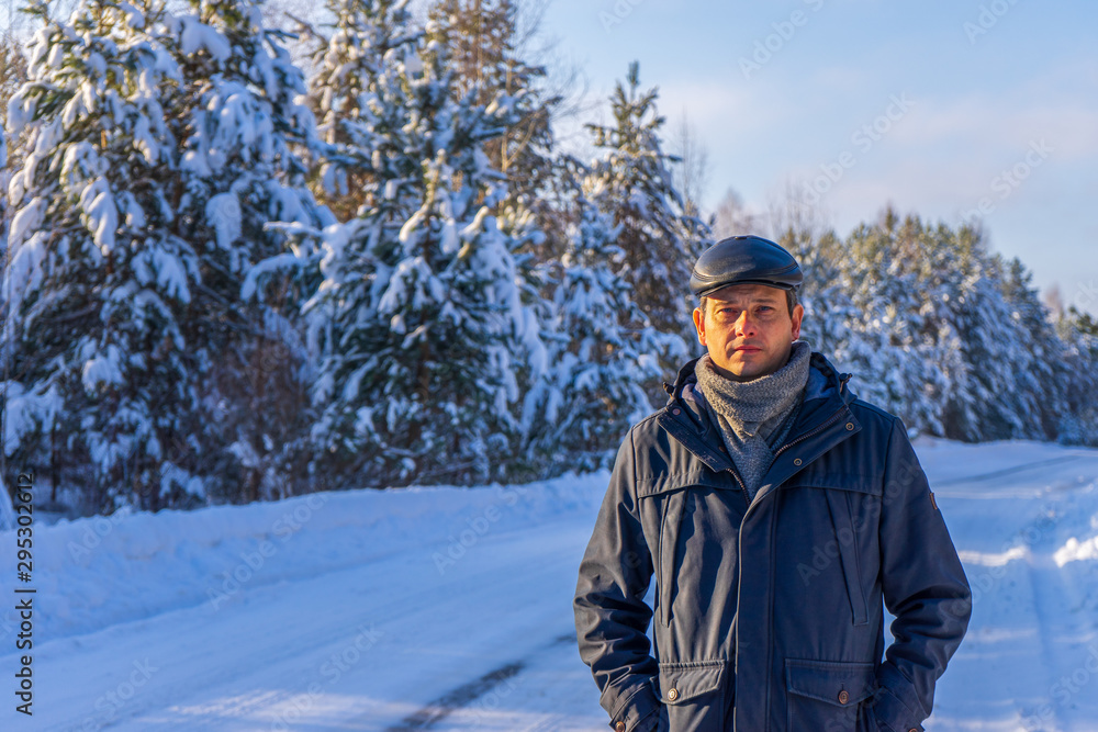 Portrait of handsome middle-aged man against beautiful winter landscape. Man walking along forest road in sunny frosty day. Human and nature, winter holidays, weekend at countryside concept Portrait of handsome middle-aged man against beautiful winter landscape. Man walking along forest road in sunny frosty day. Human and nature, winter holidays, weekend at countryside concept