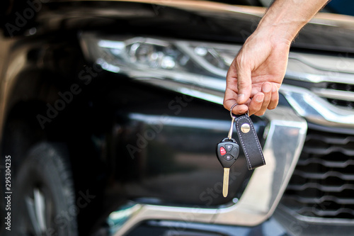 A man holding car key on black car background, journey of life concept © Yuwarin