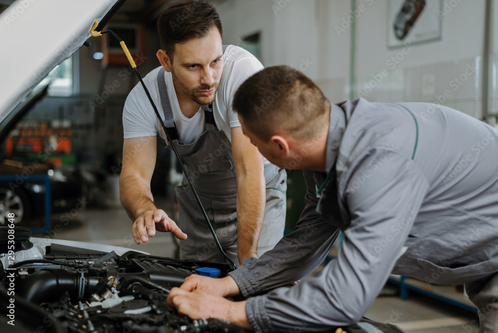 Auto mechanics talking while analyzing a car engine in a workshop Auto mechanics talking while analyzing a car engine in a workshop