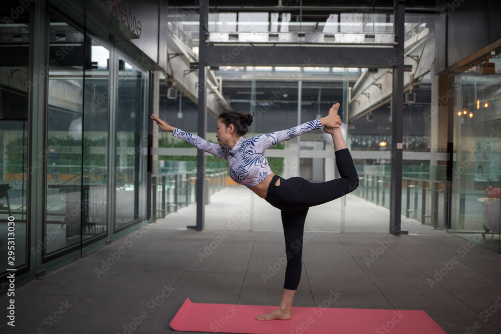 Fototapeta premium Young attractive smiling woman practicing yoga, sitting in One Legged King Pigeon exercise, Eka Pada Rajakapotasana pose, working out, wearing sportswear, grey pants, bra, indoor full length, home