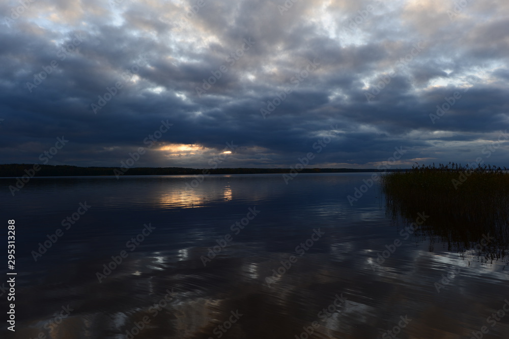 Sunlight from dark clouds at sunset reflects on the lake water