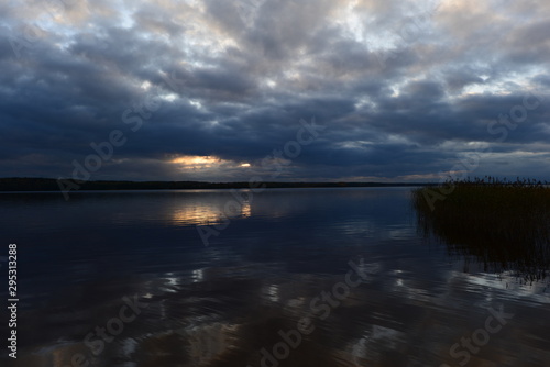 Sunlight from dark clouds at sunset reflects on the lake water