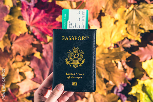 American passport with boarding pass in the woman hand maple leaves background in the autumn forest. Travel Concept. Top view. Indian summer.