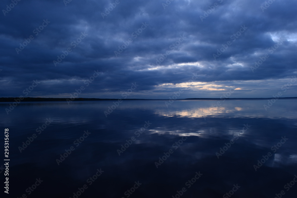 Cloudy blue sky in sunlight from dark clouds reflected on lake water