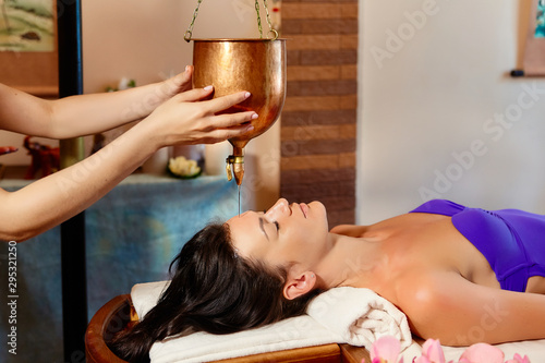 ayurveda massage alternative healing therapy.beautiful caucasian female getting shirodhara treatment lying on a wooden table in India salon