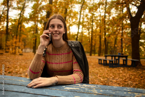  Beautiful girl emotionally speaks on the phone in the autumn park. Colorful autumn. Lifestyle.