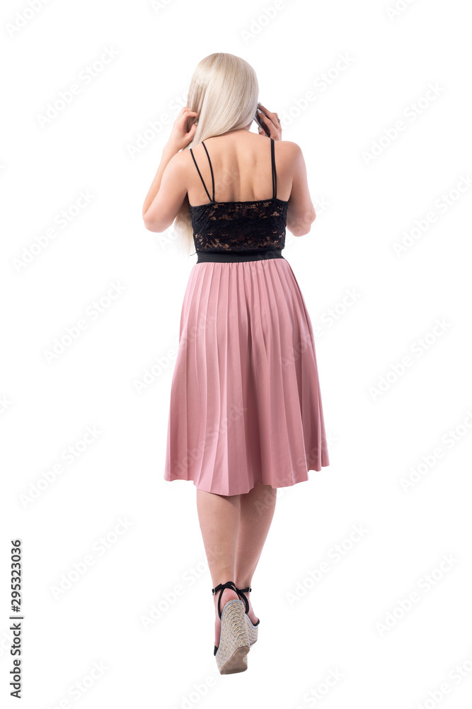 Back view of classy blonde woman in elegant clothes talking on the phone walking away. Full body isolated on white background. 
