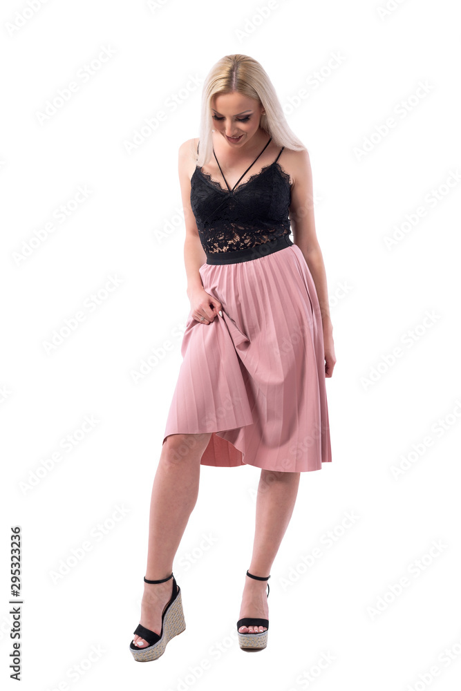 Sexy blond young adult woman lifting and raising skirt looking down and smile. Full body isolated on white background. 