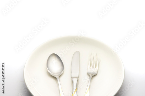fork and spoon lay on white plate on white background