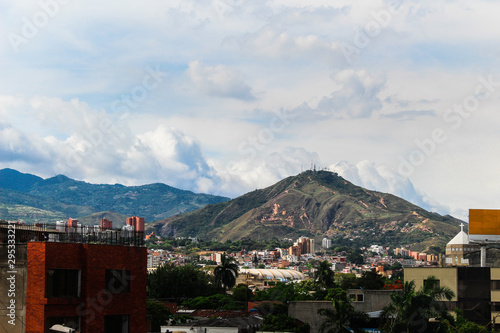 Photography of a beautiful and gorgeous landscape in the city of Cali, Colombia. The so called "hill of the three crosses" with gree mountains, a blue cloudy sky and different types of buildings. © Alternative
