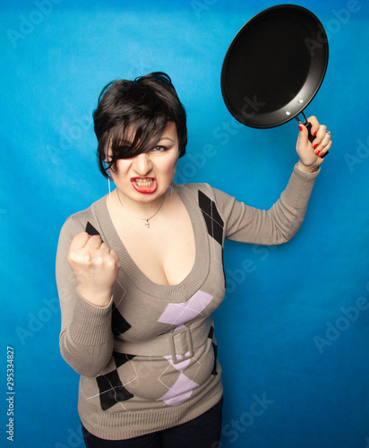 Woman beating with a frying pan on bluw studio background alone photo