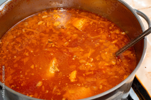Red borsch with cabbage and fat rich meat in a pan, close-up from above.