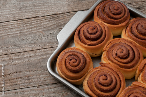 Cinnamon rolls buns on a metal baking tray on wooden table