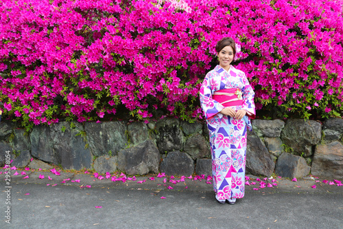 Asian beautiful woman dressing kimono and standing in front of Bougaville garden in sunny day, Kyoto Japan. The kimono is a traditional Japanese garment. photo