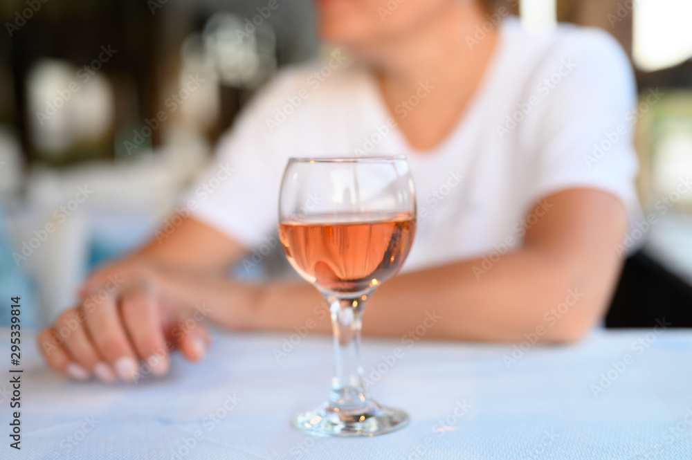 a glass of rose wine on the table in a restaurant on a blurred background of women's hands