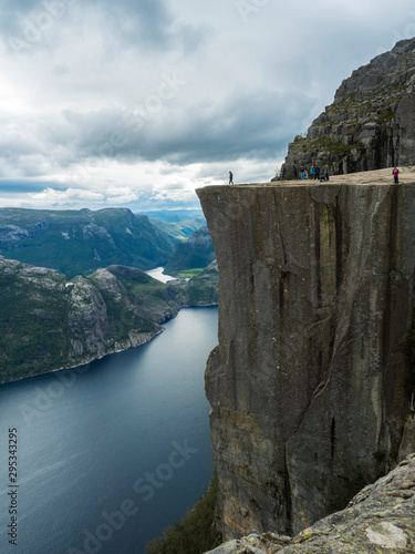 Profile view of famous Preikestolen massive cliff at fjord Lysefjord, famous Norway viewpoint with group of tourists and hikers. Moody autumn day. Nature and travel background, vacation and hiking