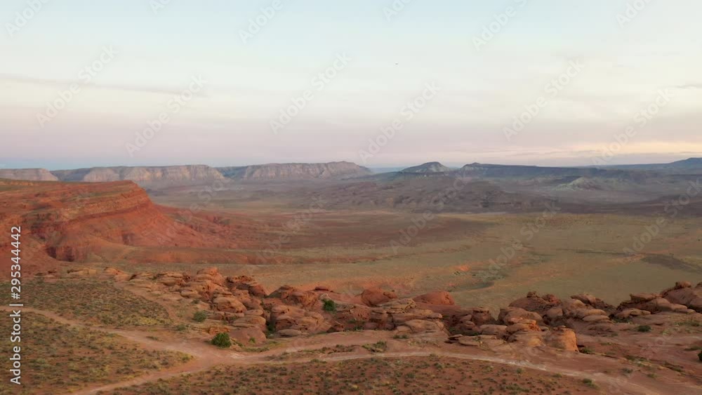 Aerial-Pulling back over rugged rocky terrain with off-road trails winding across the top of the mesa as setting sunlight enhances the red sandstone rock formations. Aerial-Pulling back over rugged rocky terrain with off-road trails winding across the top of the mesa as setting sunlight enhances the red sandstone rock formations.