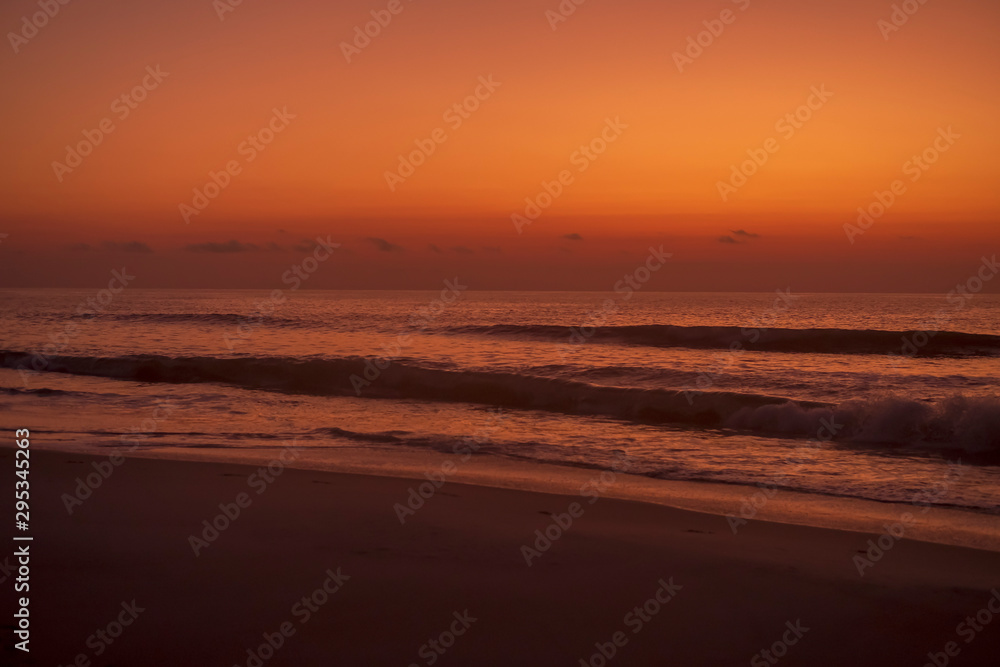 The sun rising turns the sky orange over the ocean and a beach