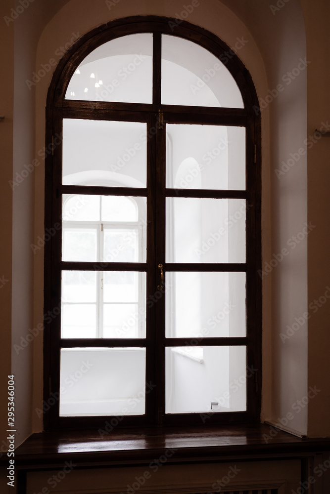 Fototapeta premium Large window with rounded top. Dark brown trims. Warm tone. Vertical orientation.