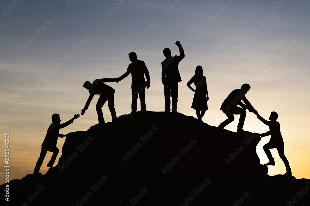 Silhouette of people helping each other hike up a mountain at sunset background. Teamwork, success and goal concept. Silhouette of people helping each other hike up a mountain at sunset background. Teamwork, success and goal concept.