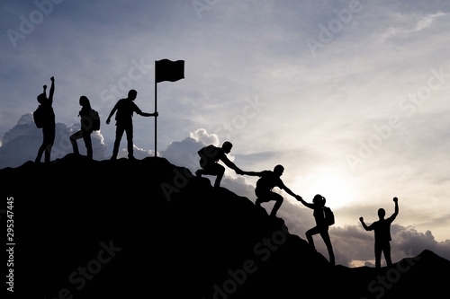 Silhouette of people helping each other hike up a mountain at sunset background. Teamwork, success and goal concept. photo