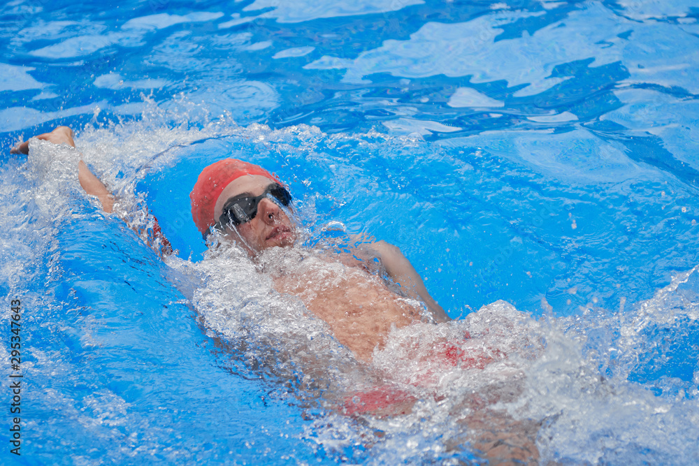 swimmer in an outdoor pool, swimming on his back, right arm raised and left down