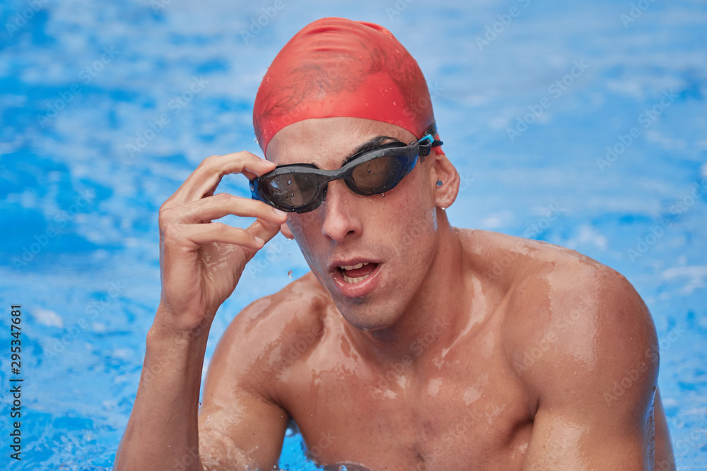 Swimmer in an outdoor pool, resting on the edge of the pool and looking at the camera, you start to take off your water goggles