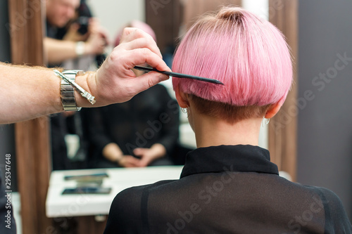 Close up of a hairdresser combs the short pink hair of her client in beauty salon. Professional hair care concept.