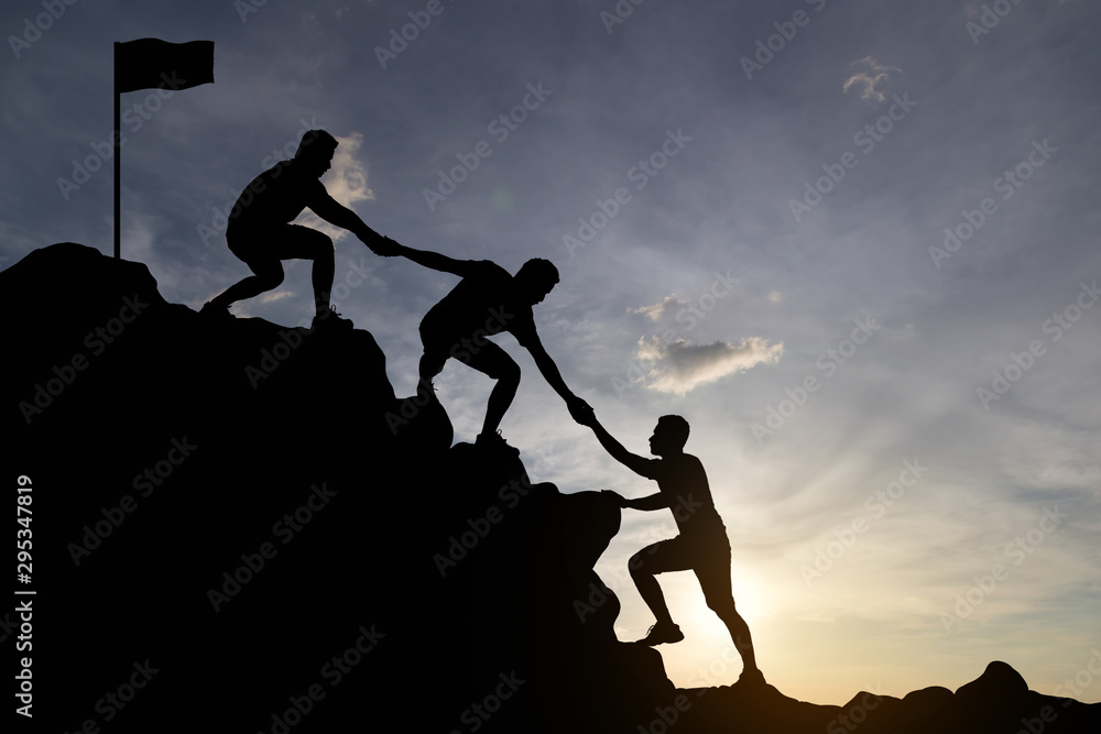 Silhouette of people helping each other hike up a mountain at sunset background. Teamwork, success and goal concept. Silhouette of people helping each other hike up a mountain at sunset background. Teamwork, success and goal concept.