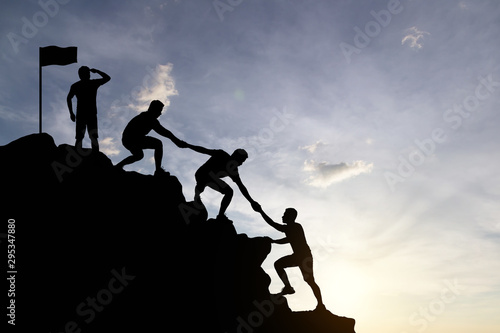 Silhouette of people helping each other hike up a mountain at sunset background. Teamwork, success and goal concept. photo