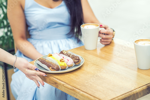 Female hand serves a plate of eclairs on a table in a cafe. The girl at the table with eclairs, a cup of coffee in the hands.