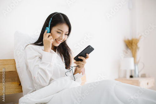 young woman relaxing and listening to music using headphones, she sitting in bed