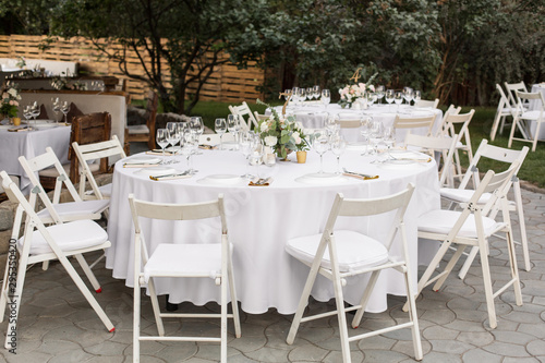 Wedding table setting decorated with fresh flowers in a brass vase. Wedding floristry. Banquet table for guests outdoors with a view of green nature. Bouquet with roses, eustoma and eucalyptus leaves