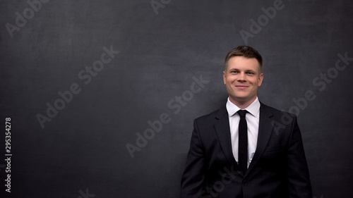 Positive businessman looking at camera, standing against black background, ad