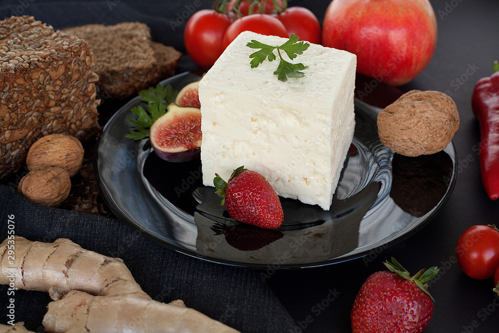 White luxury cheese, on a black plate, decorated with figs, dill and delicious strawberries, next to bread with cereals, walnuts and cherry tomatoes. The concept of cheese or healthy natural products.