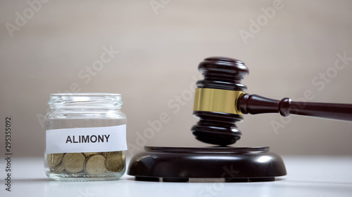 Alimony glass jar with coins on table, gavel standing on sound block, government
