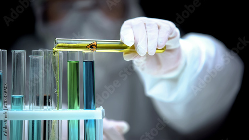 Researcher adding liquid from test tube with fire symbol, warning sign, danger photo