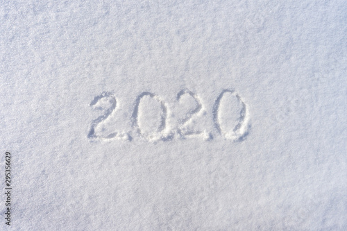 Text 2020 written on white fresh snow in sunny winter day. Merry Christmas and Happy New Year. Winter holiday concept