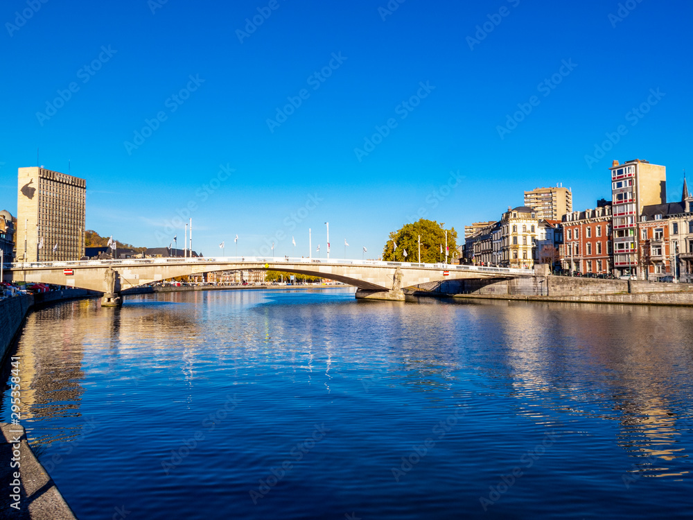 View of Meuse River and Pont des Arches bridge with water surface reflections in Liege, Belgium against a clear November sky