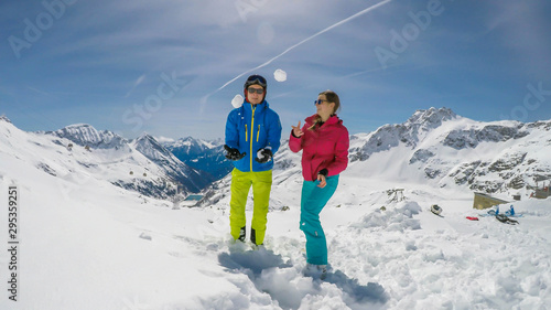 A couple in skiing outfits playing in the powder snow. They are throwing snow balls and laughing out loud, play time. Endless ranges of snow caped mountains in the back. Mölltaler Gletscher, Austria. photo