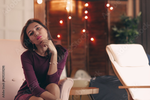 Attractive young woman resting at home in armchair, looking at camera.