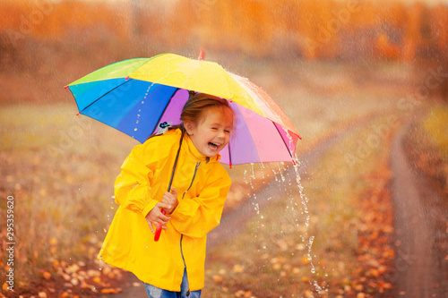 Happy girl with rainbow umbrella in autumn park