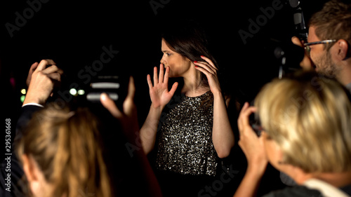 Schilderij op canvas Confused female celebrity hiding with hands from photographers cameras, news