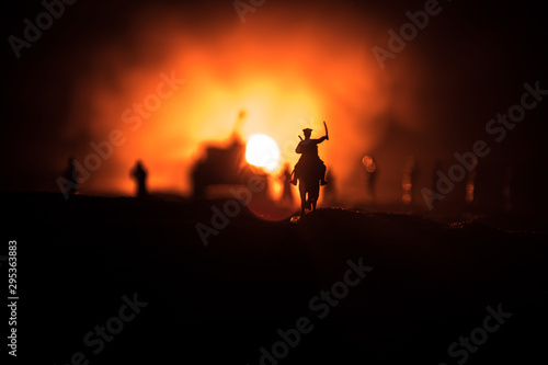 World war officer  or warrior  rider on horse with a sword ready to fight and soldiers on a dark foggy toned background. Battle scene battlefield of fighting soldiers.