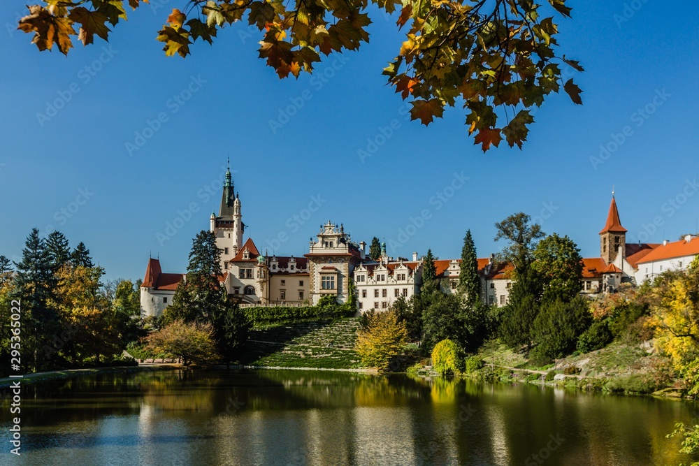 Pruhonice, Czech Republic - October 7 2019: Scenic view of famous romantic castle over a lake with its reflection in water. It is standing on hill in a public park. Sunny autumn day with blue sky. 