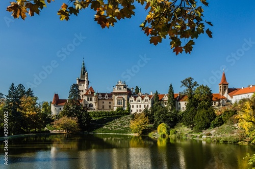 Pruhonice, Czech Republic - October 7 2019: Scenic view of famous romantic castle over a lake with its reflection in water. It is standing on hill in a public park. Sunny autumn day with blue sky. 