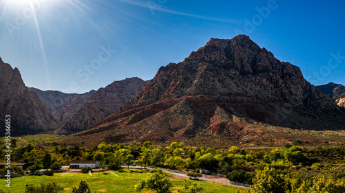 Beautiful view of famous Spring Mountain Ranch State Park near Las Vegas and Red Rock Canyon, Nevada during autumn with pink and red rock mountains, blue sky, green trees and grass, and purple hills