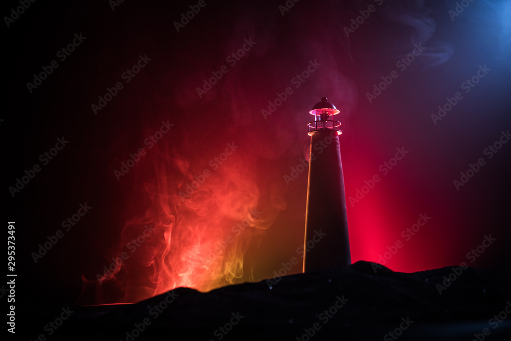 Lighthouse with light beam at night with fog. Old lighthouse standing on mountain. Table decoration. Toned background. Moonlighting.
